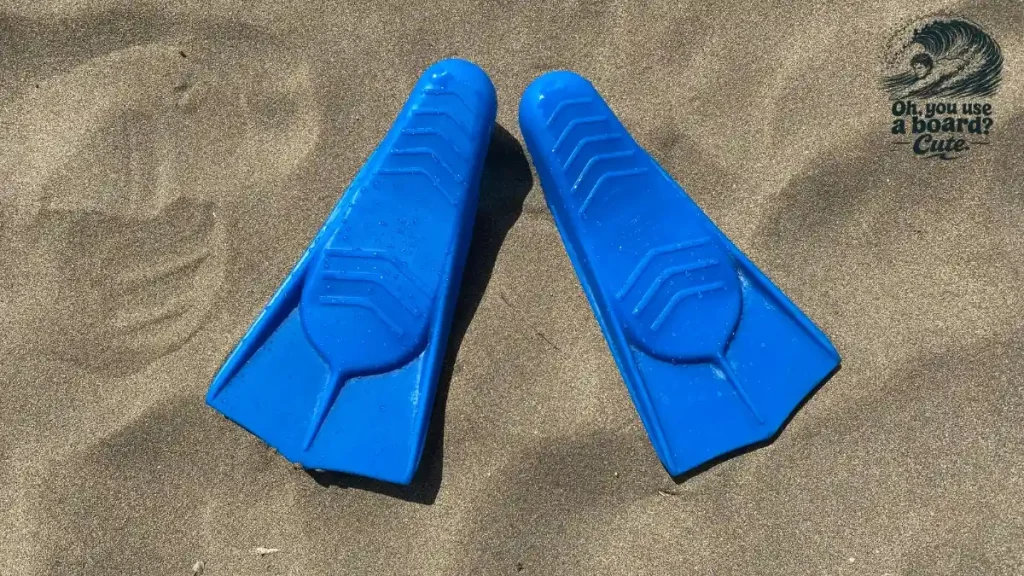 Pair of short blue swim fins lying side by side on beach sand
