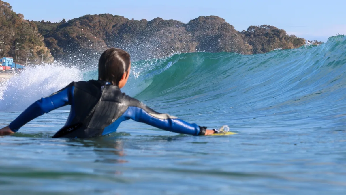 Bodysurfer in a full wetsuit holding a handplane, chest deep and facing an oncoming wave
