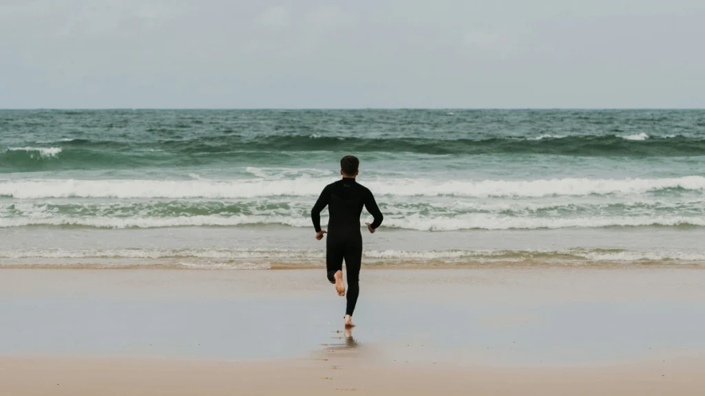 Bodysurfer in a full wetsuit running into the surf on an overcast day