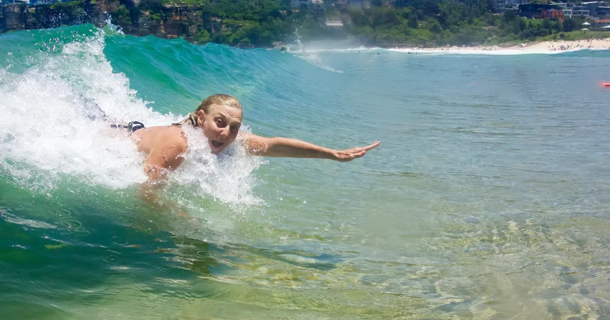 Bodysurfer riding a small clear wave with one arm extended close to shore